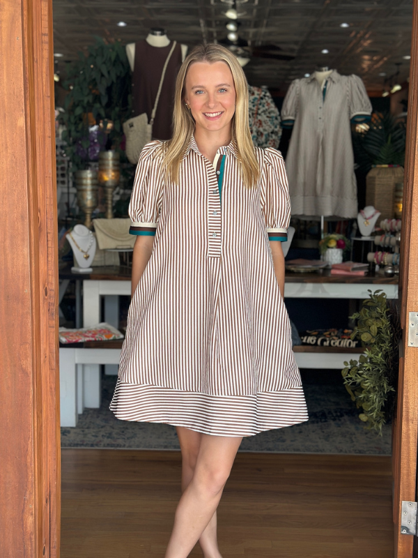 Woman wearing a striped dress standing in a store with clothing racks in the background