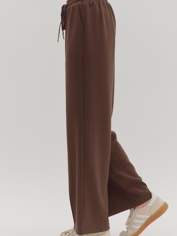 Brown pants worn with white sneakers on a light gray background