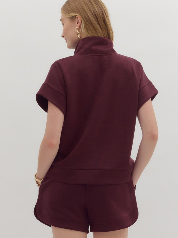 Person wearing a burgundy outfit with a matching top and shorts on a white background