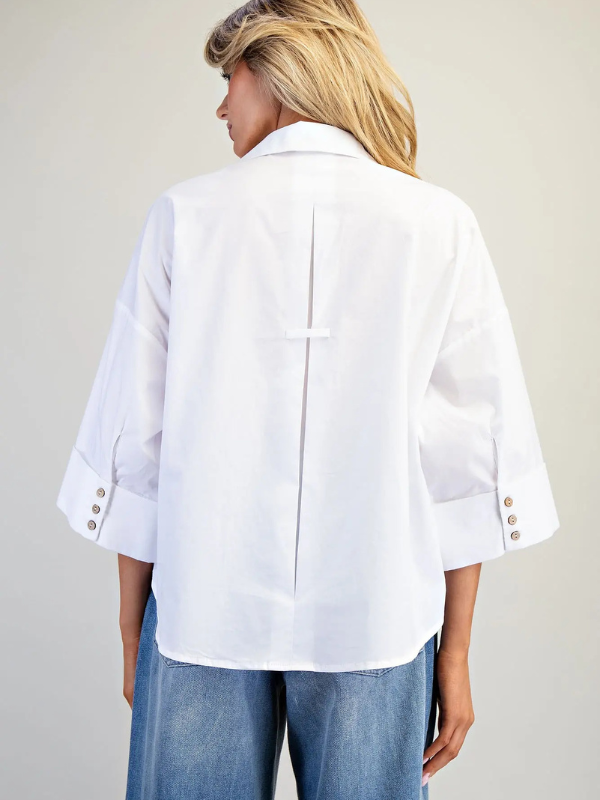 Person wearing a white blouse with rolled-up sleeves and blue jeans on a plain background