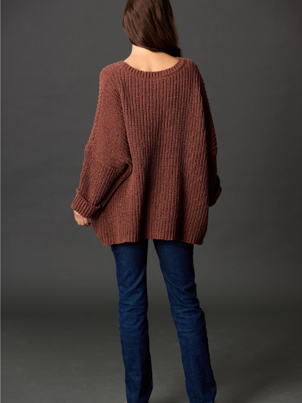 Person wearing a brown sweater and blue jeans against a gray background