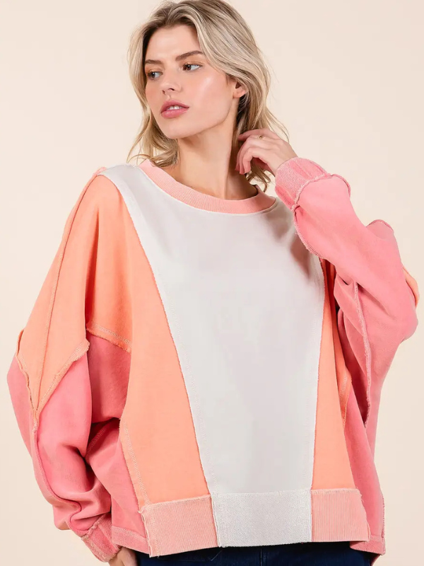 Woman wearing a colorful sweatshirt with pink, orange, and white sections on a beige background