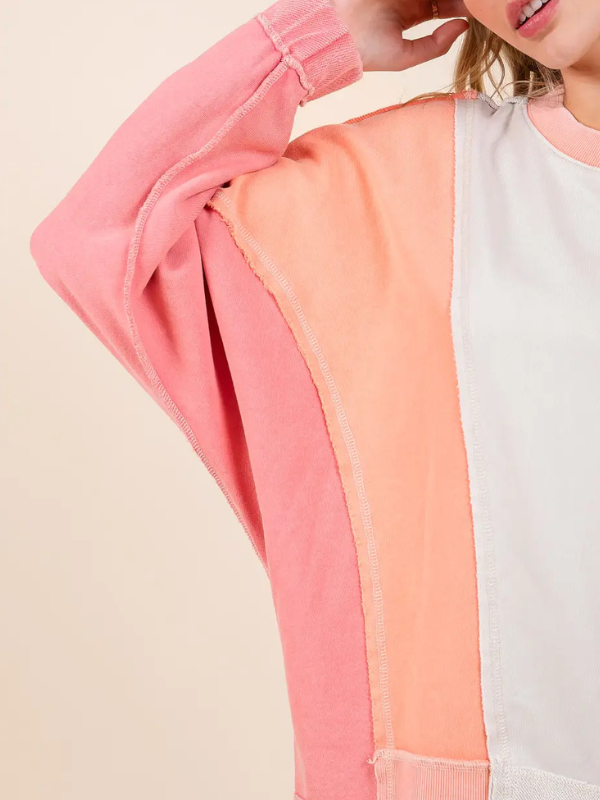 Color-blocked sweatshirt with pink, orange, and white sections on a beige background