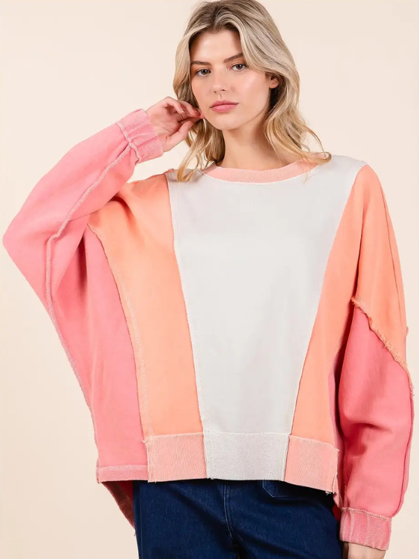 Woman wearing a colorful sweater with pink, orange, and white sections on a beige background