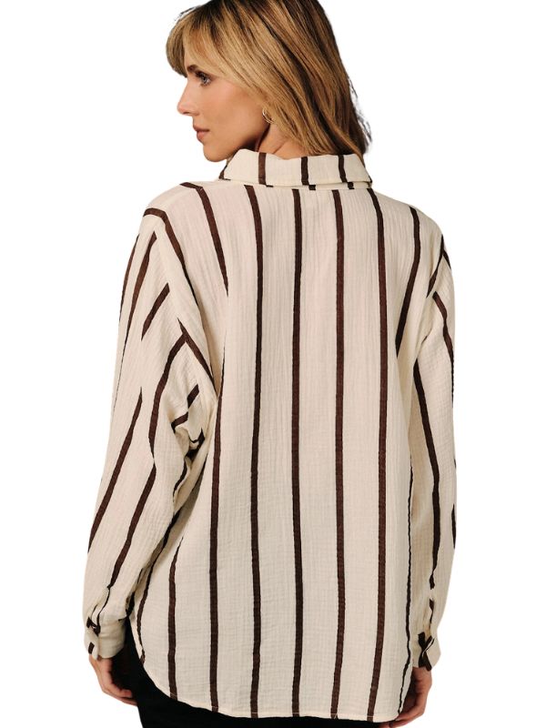 A woman shown from the back wearing a cream-colored crinkled blouse with dark brown vertical stripes, paired with black pants, against a plain white background.