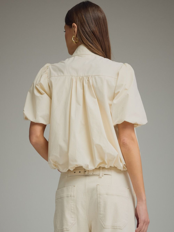 Woman wearing a cream-colored blouse with puff sleeves against a gray background