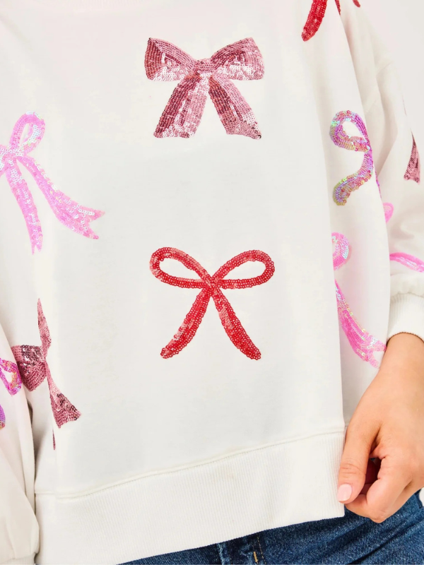 Close-up of a white sweater with pink and red bow patterns.