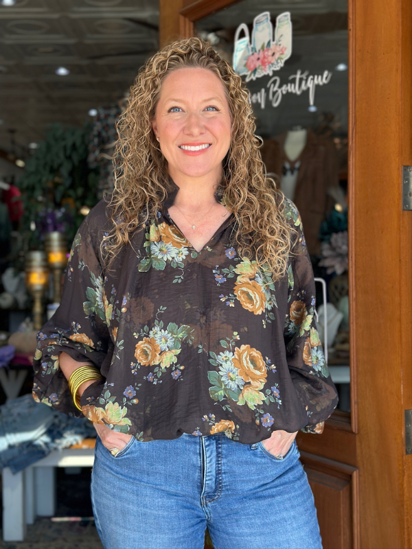 Woman wearing a floral blouse and jeans standing in front of a store entrance.