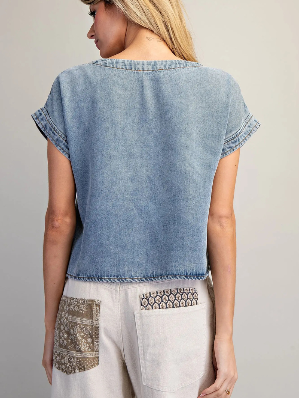 Woman wearing a denim top with white pants featuring patterned pockets on a gray background