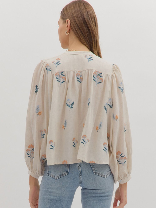 Woman wearing a beige blouse with floral patterns and light blue jeans on a white background