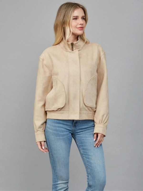 Woman wearing a beige jacket and blue jeans on a gray background