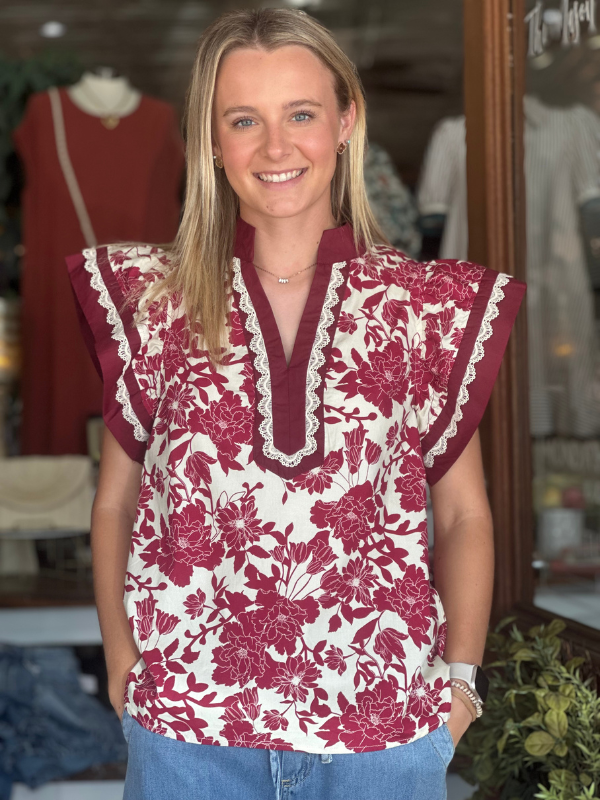 Woman wearing a floral blouse with maroon and white pattern in a clothing store.