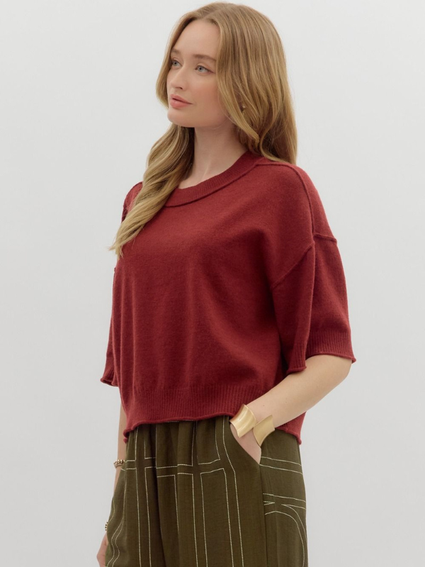 Woman wearing a red sweater and green pants on a plain background