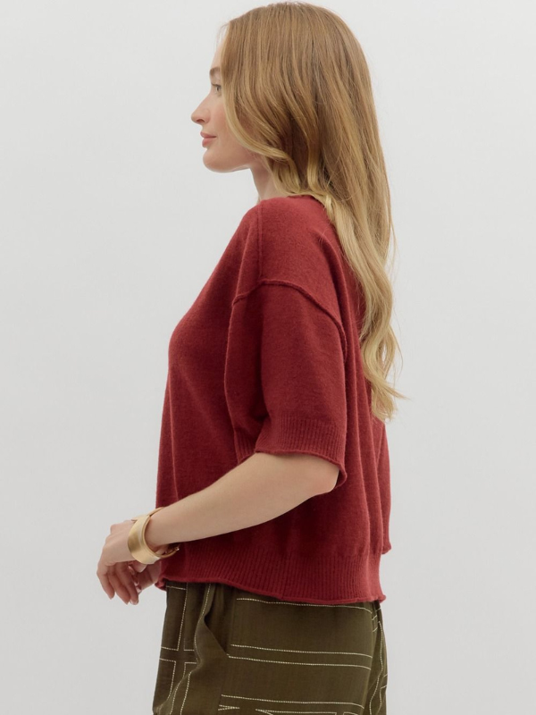 Woman wearing a red sweater and green pants against a white background