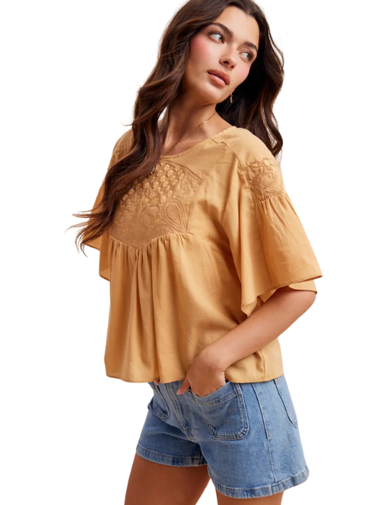 Woman wearing a mustard yellow blouse with lace details and denim shorts on a white background