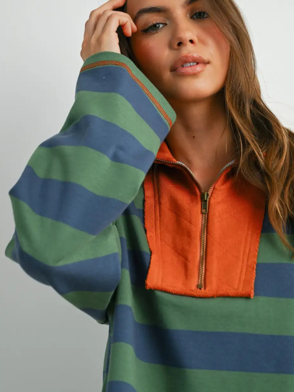 Woman wearing a green and blue striped sweater with an orange zipper.