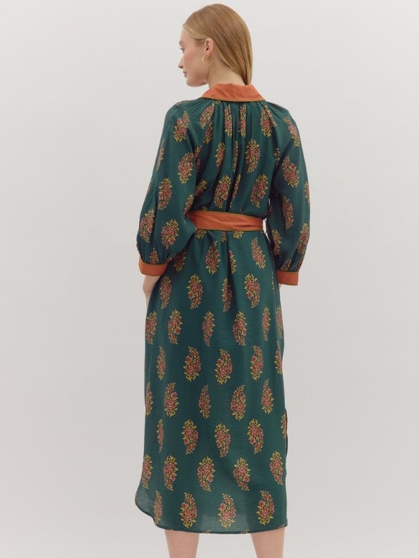 Woman wearing a green patterned dress with orange accents on a white background