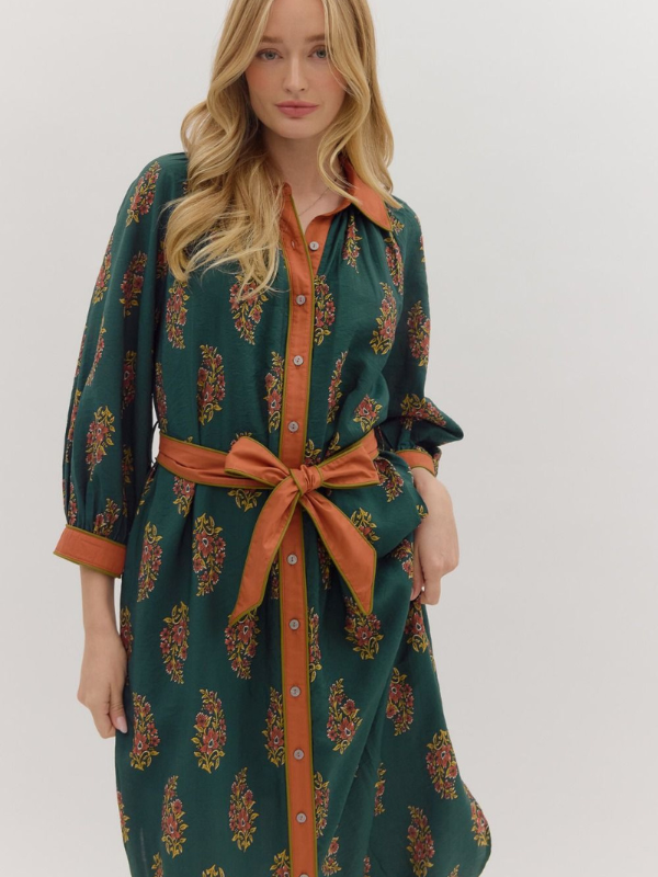 Woman wearing a green dress with orange accents and a belt on a white background