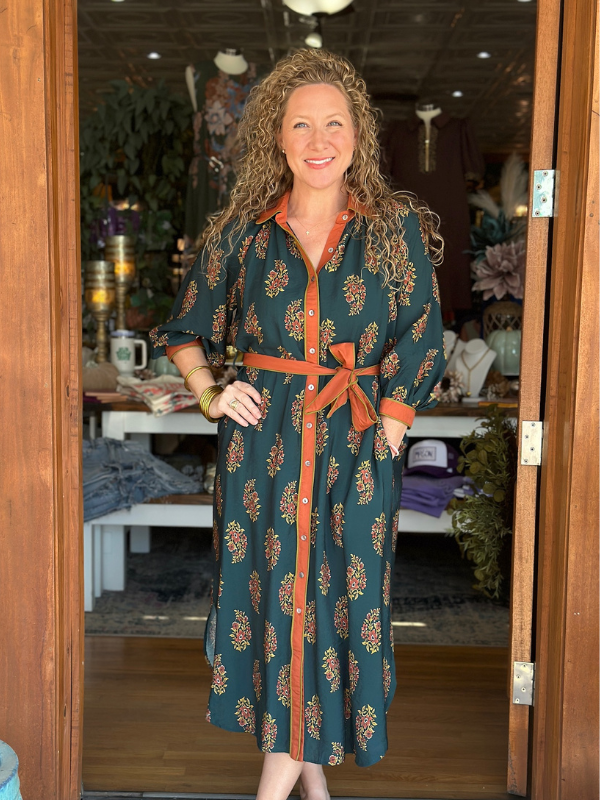 Woman in a patterned dress standing in a doorway with a store interior in the background