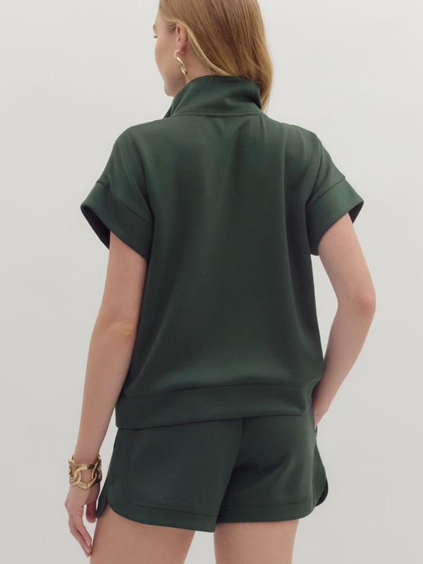 Person wearing a green polo shirt and shorts set on a plain background