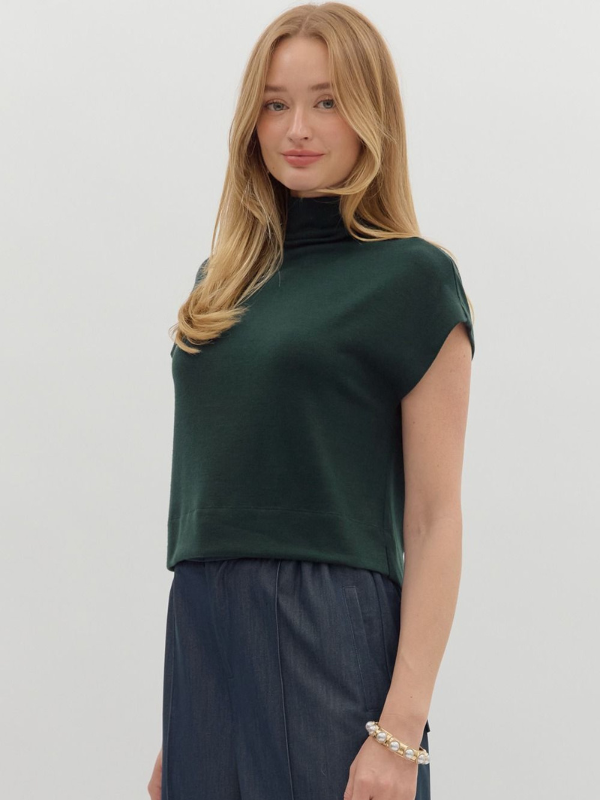 Woman wearing a green top and dark pants against a plain background