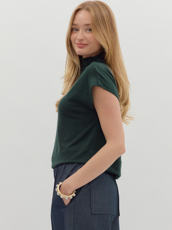Woman wearing a green top and dark pants against a white background