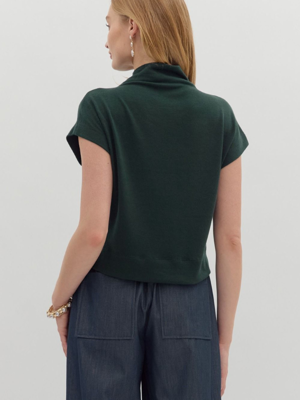 Person wearing a green top and dark pants on a plain background