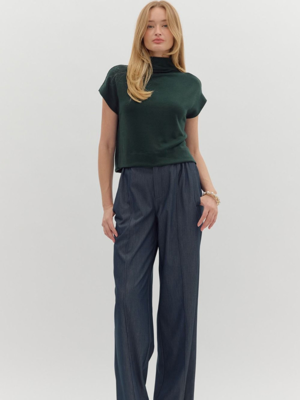 Woman wearing a green top and dark pants on a white background