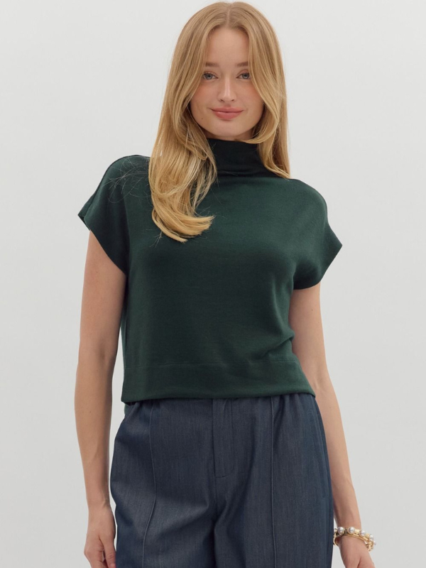 Woman wearing a green top and dark pants against a white background