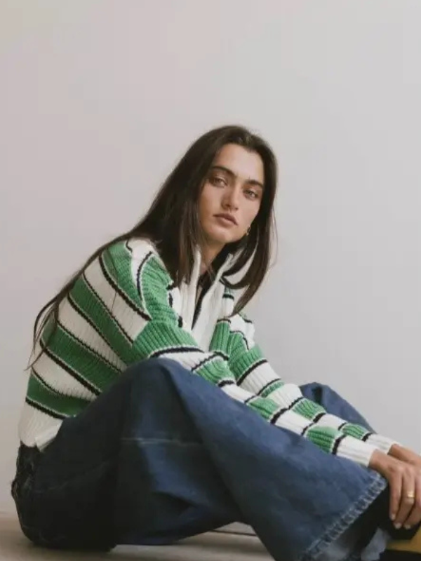 Person wearing a green and white patterned sweater sitting on the floor against a plain background