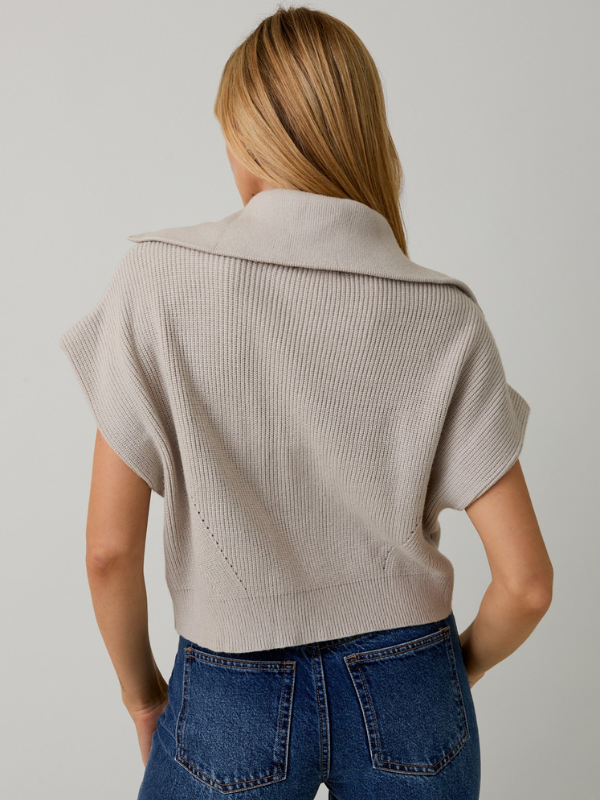 Person wearing a beige short-sleeve cardigan over a blue top against a plain background