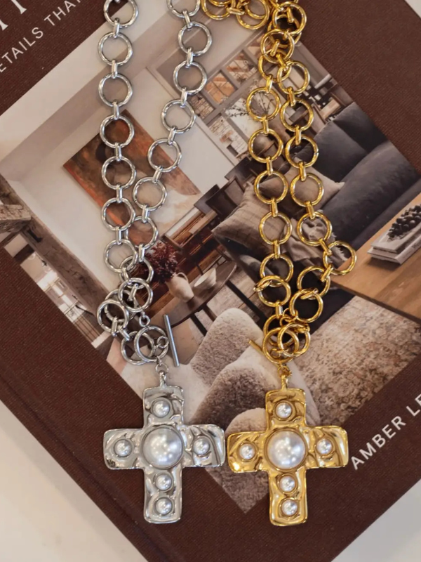 Two cross-shaped pendants on gold and silver chains against a blurred magazine background.