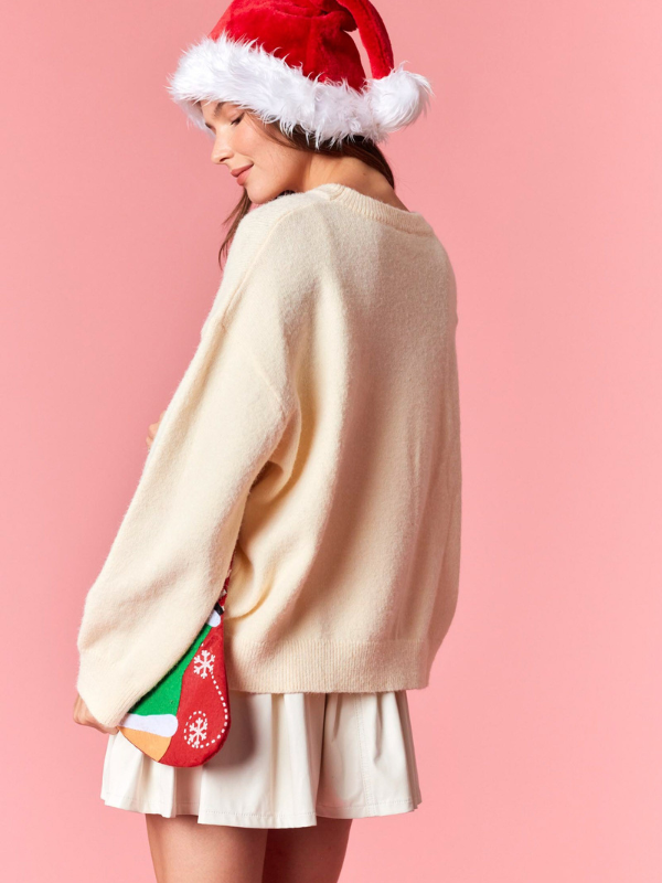 Person wearing a beige sweater, white skirt, and Santa hat with a colorful bag on a pink background