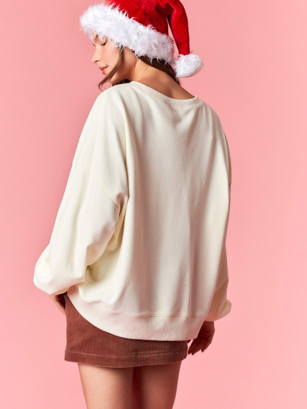 Person wearing a white oversized sweater and brown shorts with a Santa hat on a pink background