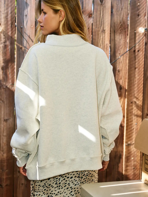 Person wearing a light gray sweatshirt in front of a wooden fence