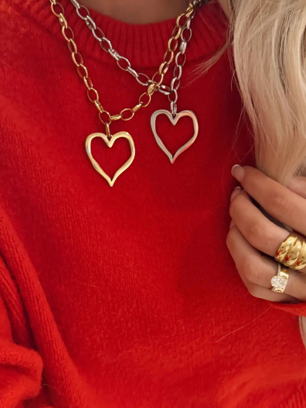 Person wearing a red sweater with gold and silver heart-shaped pendants on a necklace.