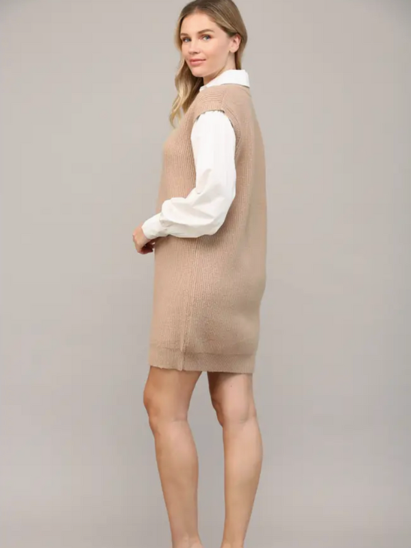 Woman wearing a beige knitted vest over a white shirt on a plain background
