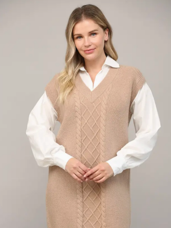 Woman wearing a beige knitted vest over a white shirt against a plain background