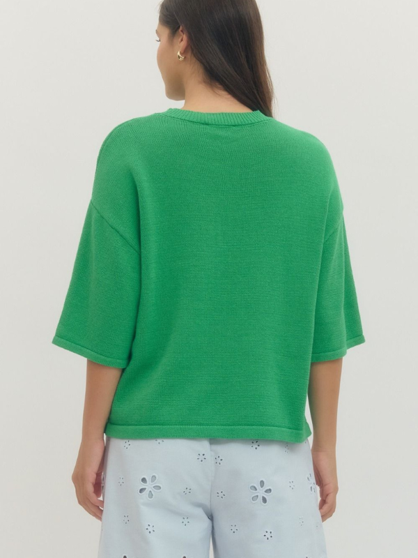 Person wearing a green oversized shirt with light-colored pants on a plain background