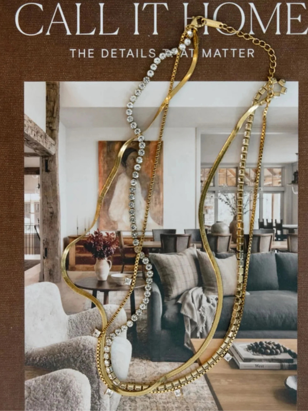 Decorative gold necklaces on a magazine cover with a blurred living room background