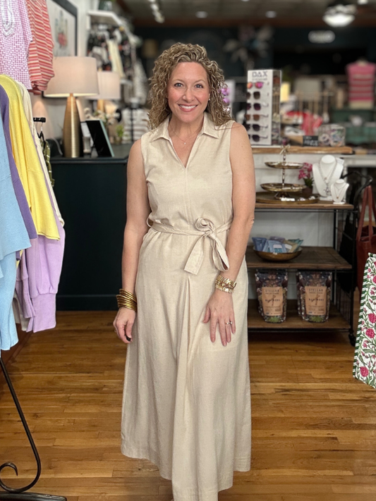 Woman in a beige dress standing in a store with clothing and products in the background