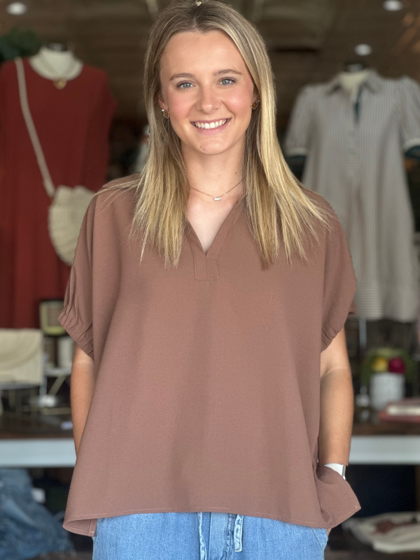 Woman wearing a brown blouse and blue jeans in a clothing store.