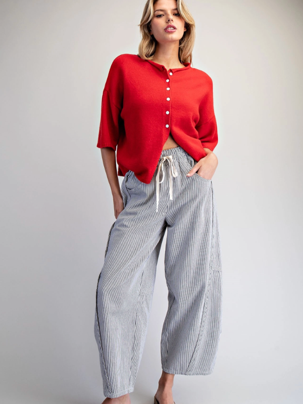 Woman wearing a red sweater and gray striped pants on a plain background