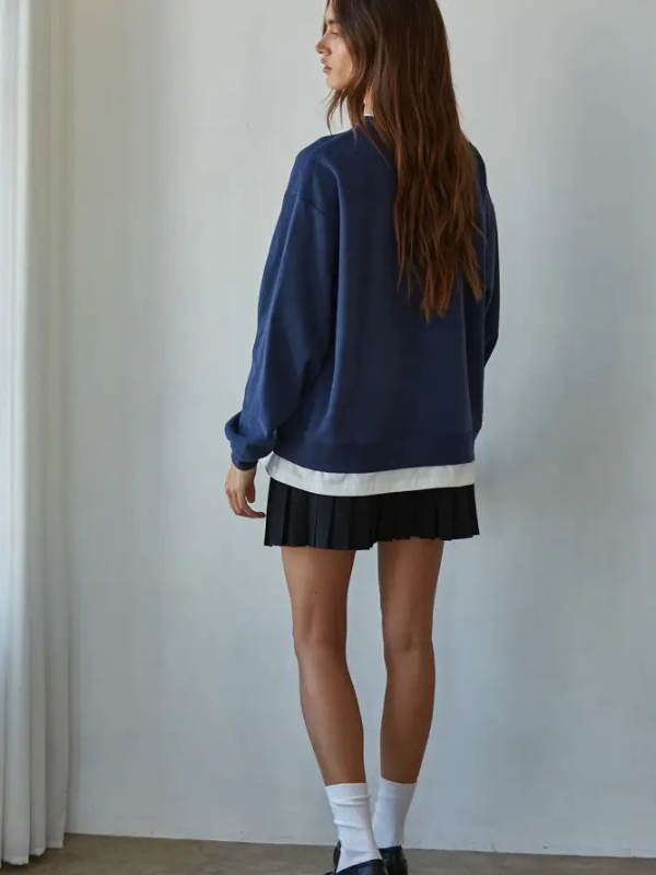 Person wearing a blue sweater and black pleated skirt against a plain background