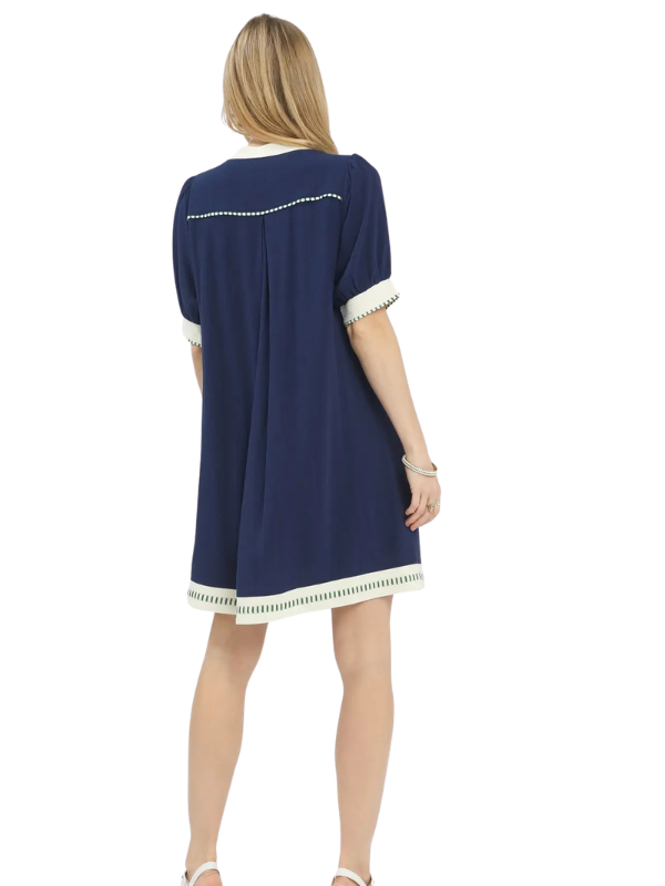 A woman viewed from the back wearing a navy blue short-sleeve shift dress with white contrast trim at the collar, sleeve cuffs, and hem.