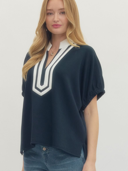 Woman wearing a navy blue top with a white V-neckline on a plain background