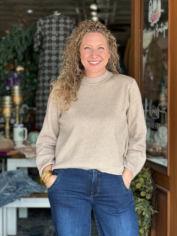 Woman wearing a beige sweater and blue jeans standing in a store.