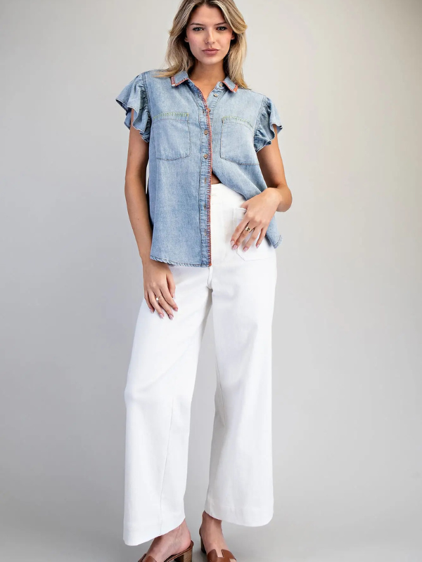 Woman wearing a denim shirt and white pants on a plain background