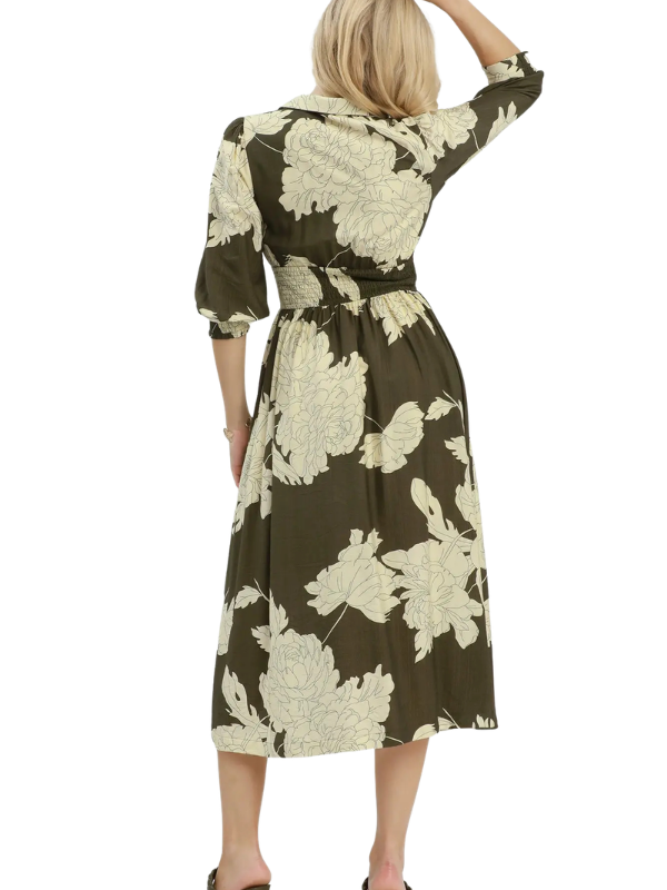 A woman shown from the back wearing a knee-length collared dress with three-quarter sleeves and a matching waist tie. The dress has a dark olive-brown base with a large cream floral print.