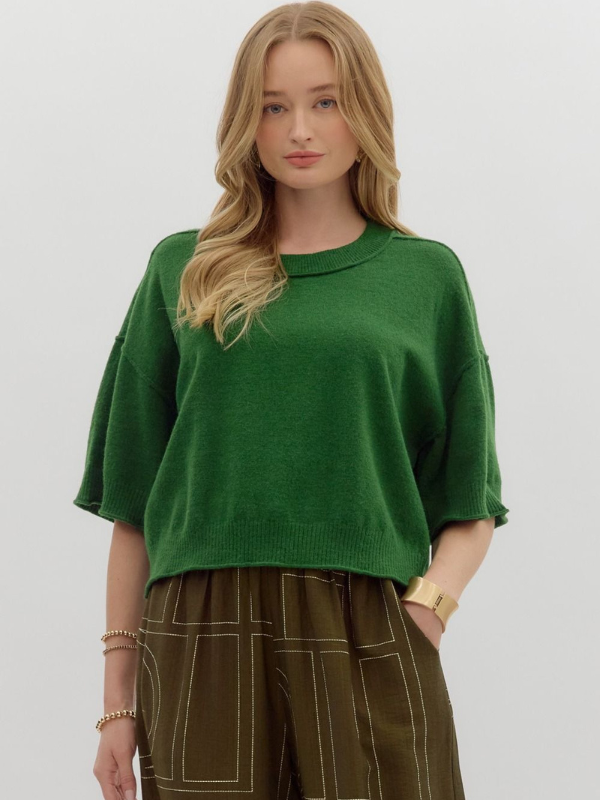 Woman wearing a green sweater and brown pants on a white background